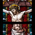 Detailed stained glass depiction of the crucifixion featuring Christ and religious icons.