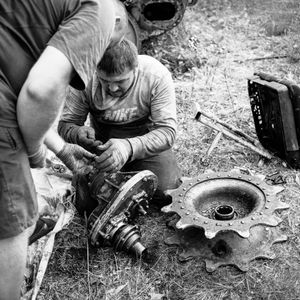 Two men repairing machinery outdoors, showcasing teamwork and mechanical skills.